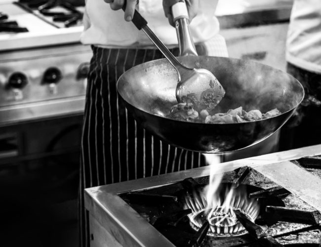 Chef cooking with flame in a frying pan on a kitchen stove